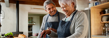 Older couple smiling while preparing food together in a cozy kitchen